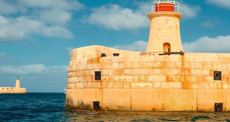 Lighthouse and fortifications by the seaside under a blue sky.