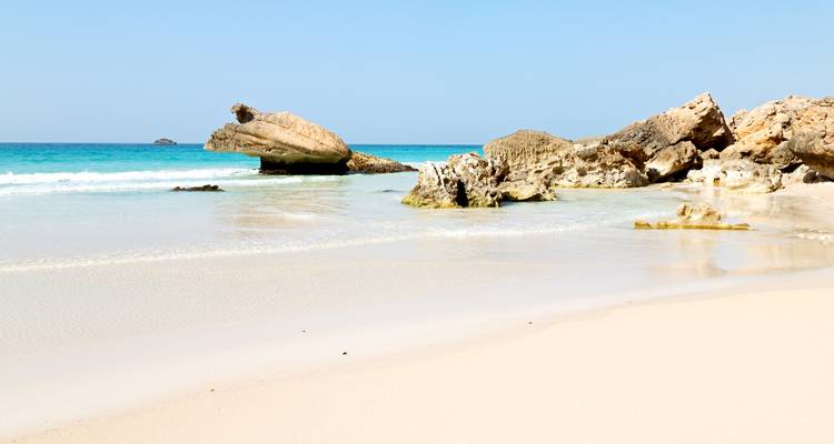 Playa de arena blanca pristina con formaciones rocosas únicas y suaves olas turquesas.