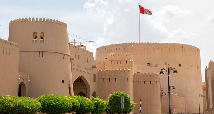 Beeindruckende kreisförmige Wüstenfestung mit omanischer Flagge, die bei teilweise bewölktem Himmel oben weht.