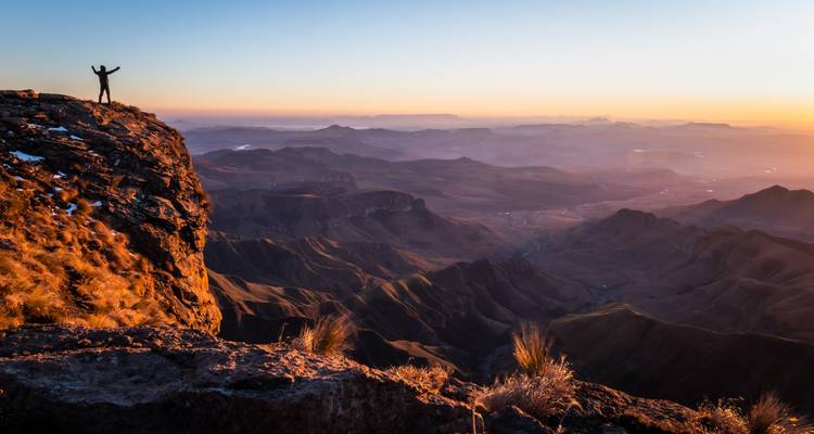 Persoon die triomfantelijk op een klif staat bij zonsopgang.