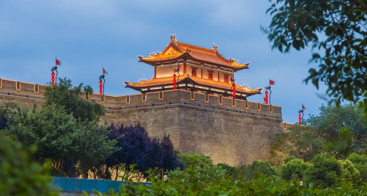 Illuminated ancient tower atop Xi’an city wall standing above fortified brick ramparts at dusk.