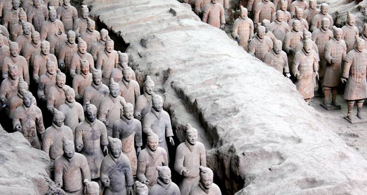 Rows of life-size Terracotta Warriors and horses standing in excavated pits inside museum.