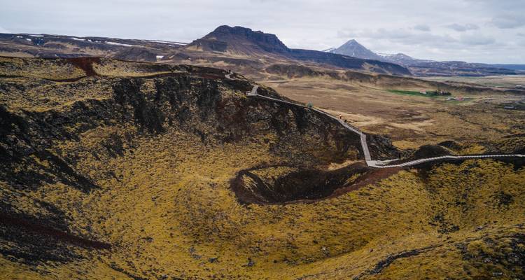 Ein gewundener Holzweg verläuft entlang des Randes eines massiven Vulkankraters inmitten der rauen isländischen Landschaft.
