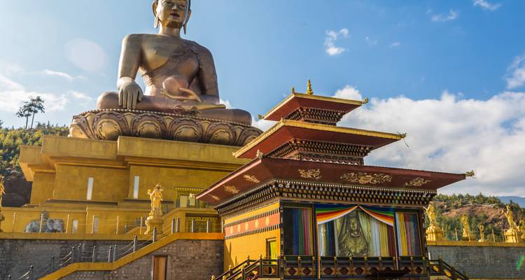 Große goldene Buddha-Statue und ein Tempel mit Bergen im Hintergrund.