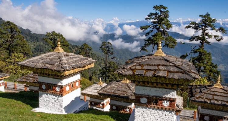 Traditionelle bhutanische Stupas in einer Landschaft mit wolkenverhangenen Bergen.