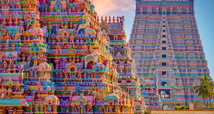 Vibrantly painted South Indian temple gopurams adorned with deities under pastel sky.
