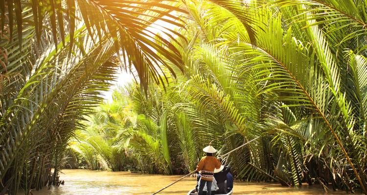 Persona en un barco tradicional navegando por un canal verde y exuberante.