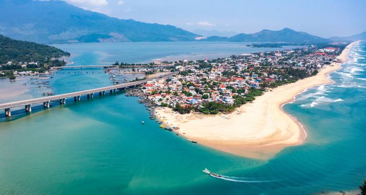 Vista aérea de un pueblo costero con un puente y montañas de fondo.