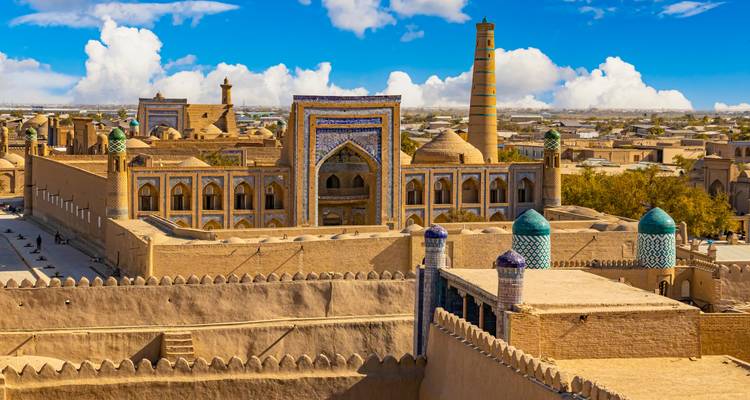 Panoramablick auf die antike ummauerte Stadt Chiwa mit Minaretten, Medresen und sandfarbenen Gebäuden unter blauem Himmel.