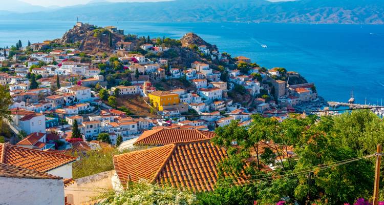 Weiße Häuser mit Terrakotta-Dächern ergießen sich von einem felsigen Vorsprung hinab zu einem tiefblauen Meer.
