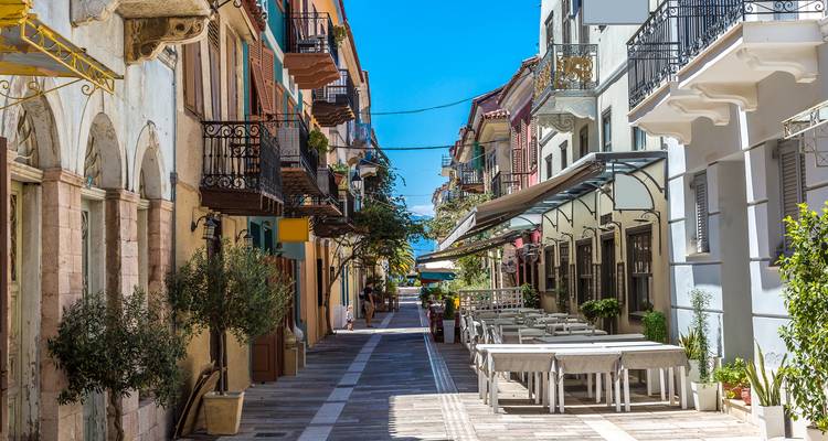 Charmante Fußgängerzone mit bunten Balkonen, Cafés und Steinfassaden in einer griechischen Altstadt.
