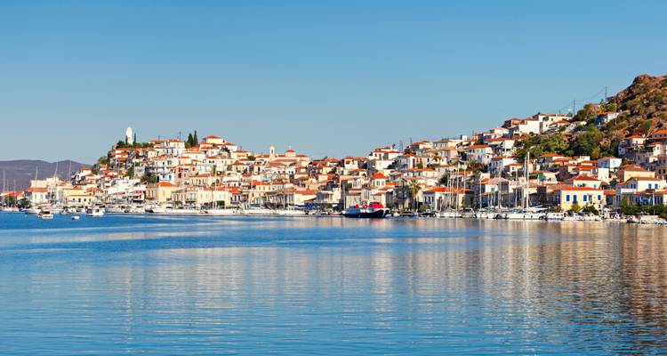 Küstenstadt erstreckt sich entlang ruhigen Wassers mit Spiegelungen von weißen und terrakottafarbenen Gebäuden.