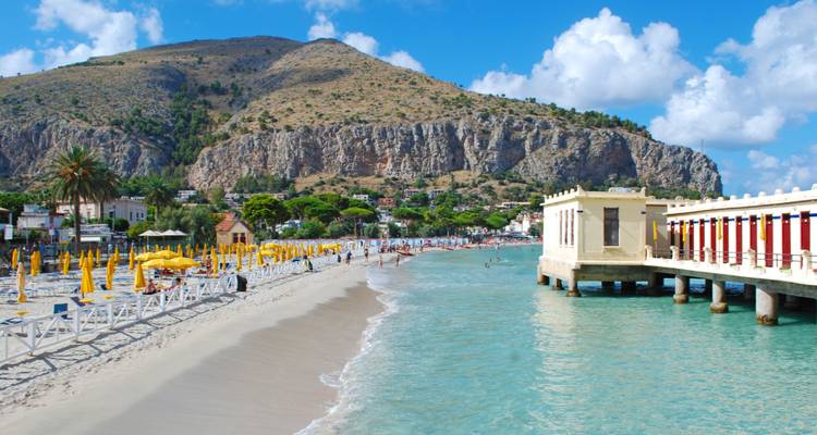 Turquoise wateren en zandstrand van Mondello met historische pier en bergachtergrond.