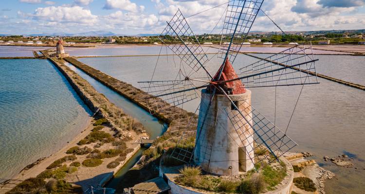 Historische windmolen met uitzicht op glinsterende zoutpannen en kustlandschap in west-Sicilië.