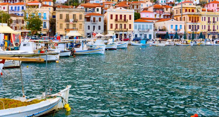 Buntes Hafendorf mit vertäuten Fischerbooten und pastellfarbenen Häusern, die sich im kräuselnden Wasser spiegeln.