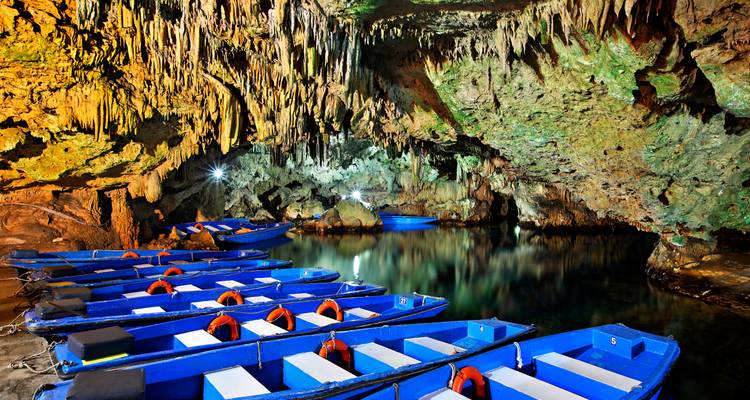 Reihen von leuchtend blauen Ausflugsbooten schwimmen auf einem stillen unterirdischen See unter dramatischen Stalaktiten in einer Höhle.