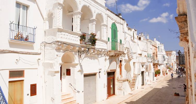 Une ruelle étroite blanchie à la chaux bordée de balcons baroques ornés et de volets verts baigne dans le soleil éclatant des Pouilles.