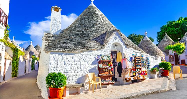 Des maisons trulli emblématiques aux toits coniques en pierre se dressent sous un ciel bleu éclatant à Alberobello, ornées d'artisanat local.
