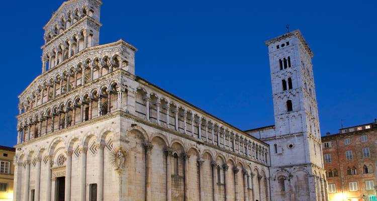 Die verzierte romanische Fassade und der Glockenturm von San Michele in Foro leuchten gegen einen tiefblauen Abendhimmel in Lucca.