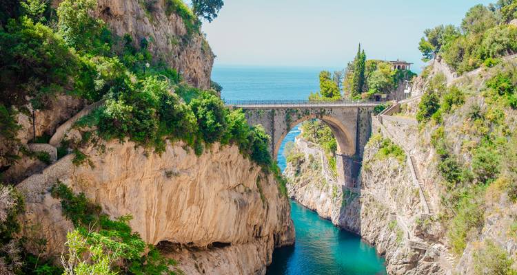 Die dramatische Steinbogenbrücke des Fiordo di Furore überspannt eine schmale türkisfarbene Bucht, die zwischen hohen Kalksteinfelsen und üppiger Vegetation liegt.