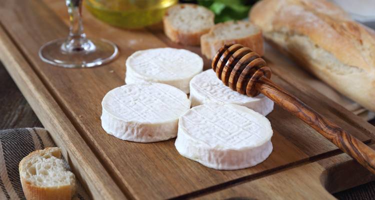 Rustikale Käseplatte mit Ziegenkäse-Talern, Baguettescheiben, Honiglöffel und einem Glas Wein.