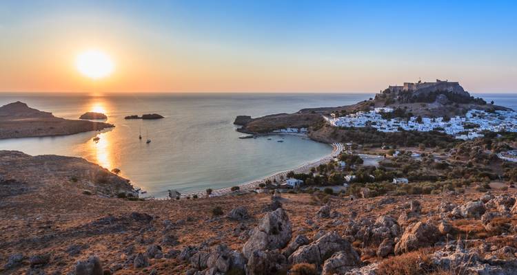 Coucher de soleil doré sur une baie en croissant avec une acropole antique et un village aux murs blanchis à la chaux.