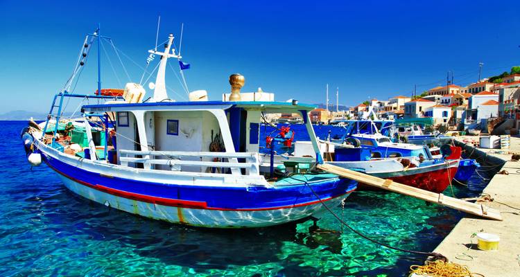 Des bateaux de pêche colorés amarrés dans un port aux eaux cristallines à côté de maisons blanches.
