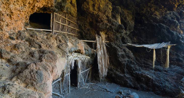 Habitation troglodytique rustique avec nattes de roseau et supports en bois construite dans la roche volcanique.