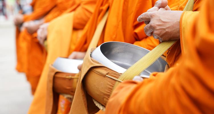 Nahaufnahme von buddhistischen Mönchen in orangefarbenen Roben, die silberne Almosenschalen während eines Morgenrituals halten.
