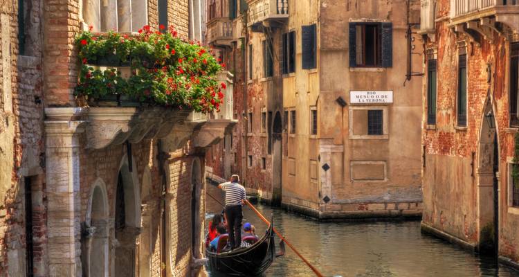 Gondoliere, der ein Boot durch einen schmalen Kanal lenkt, gesäumt von blumengeschmückten Balkonen in Venedig