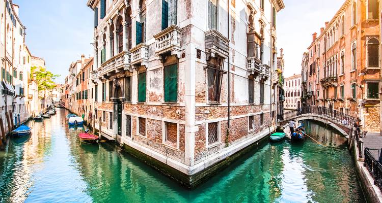 Hell erleuchteter Eckpalazzo, der sich im smaragdgrünen Wasser des Venediger Kanals zwischen zwei schmalen Wasserwegen spiegelt