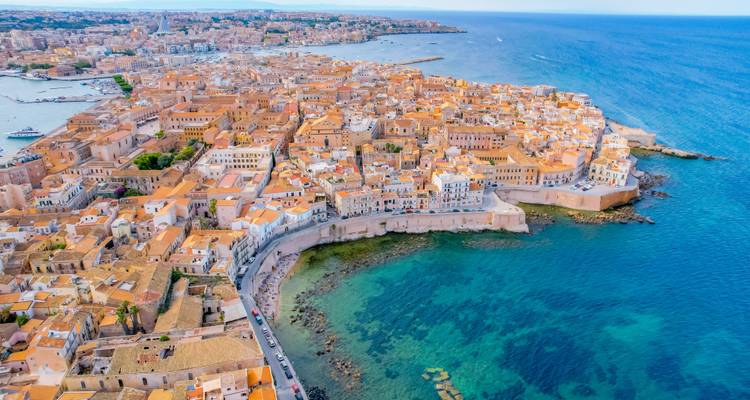 Luftaufnahme der Insel Ortigia in Syrakus mit Terrakotta-Dächern, mittelalterlichen Mauern und türkisfarbenem Wasser.