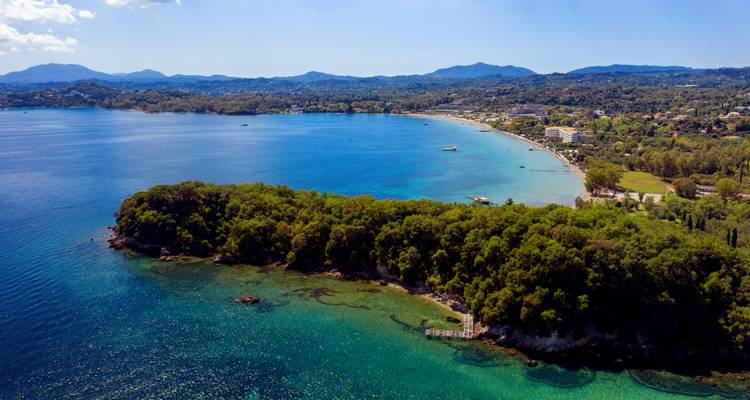 Vista aérea de un promontorio boscoso que se adentra en un mar azul profundo con una larga costa arenosa más allá.