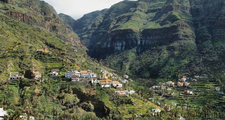 Weelderig terrasdorp genesteld in een dramatische groene kloof onder torenhoge vulkanische kliffen op La Gomera.