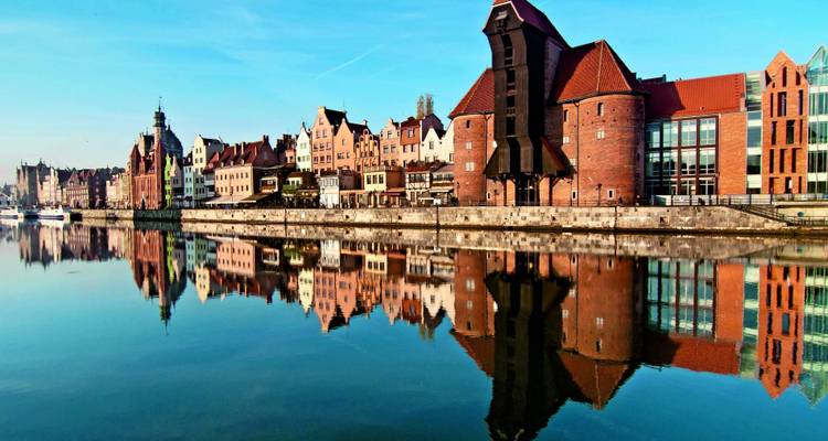 Städtische Uferpromenade mit historischen Gebäuden, die sich im Wasser spiegeln.