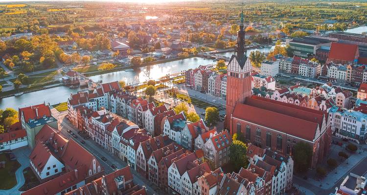Luftaufnahme bei Sonnenuntergang einer alten Stadt mit farbenfrohen Dächern, Kanälen und einem hohen Kirchturm in Elbląg, Polen.