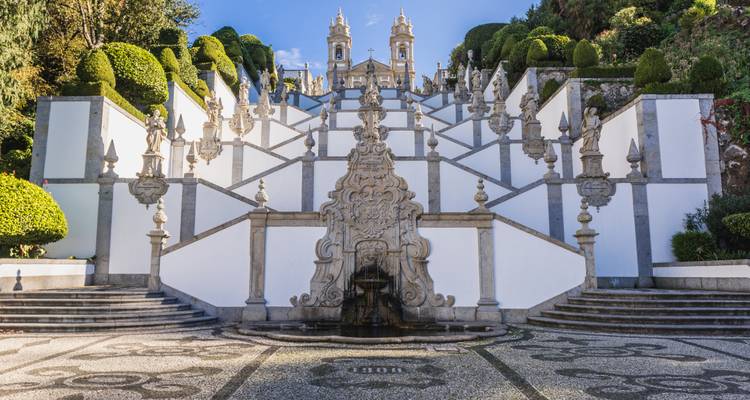 Grand escalier baroque avec des statues ornées menant à une église aux deux tours jumelles sous un ciel bleu.