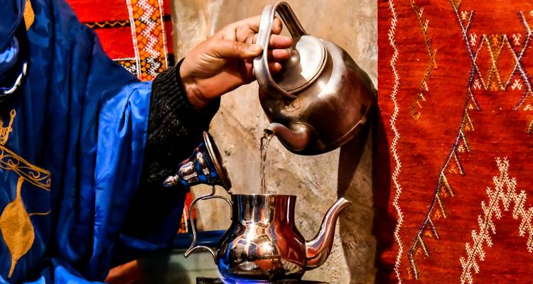 Person, die Tee aus einer Metallkanne in eine andere gießt.