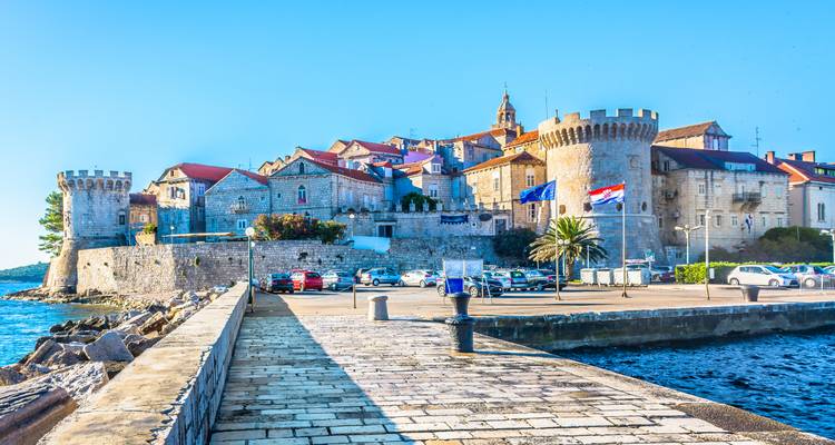 Stone walls and round towers of Korčula Old Town rising above the waterfront on a bright day