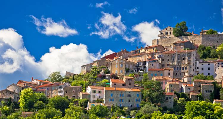 Hill-top medieval village of Motovun with stone houses and red roofs set against a vivid blue sky and white clouds