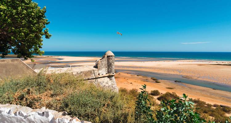 Vista de una playa arenosa con océano azul y antigua fortificación.