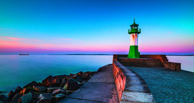 Farbenfroher Sonnenuntergang über einem Leuchtturm am Meer.
