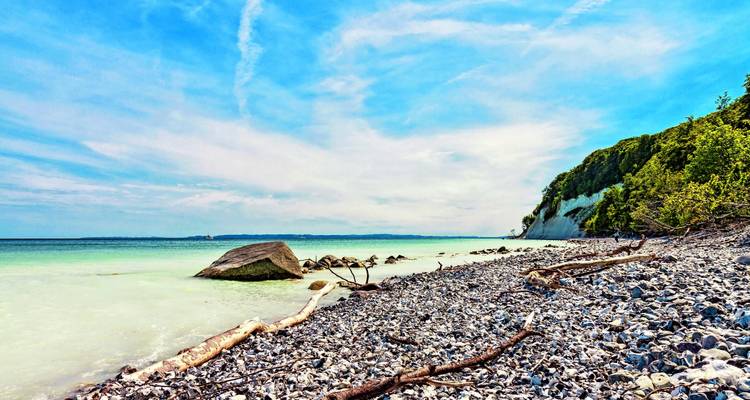 Kiesstrand mit Klippen und klarem Wasser.