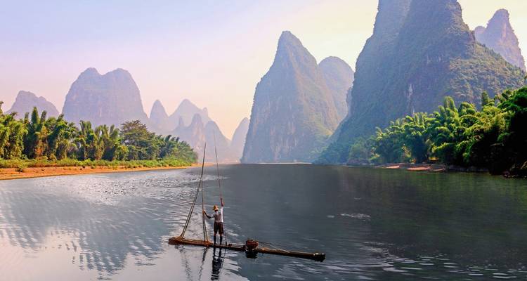 Visser op bamboevlot met dramatische karstbergen op de achtergrond.
