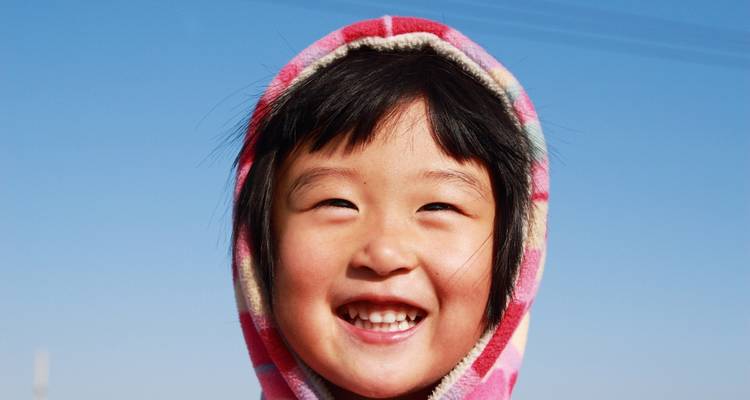 Kleines Kind mit bunter Kapuze, das breit lächelt.