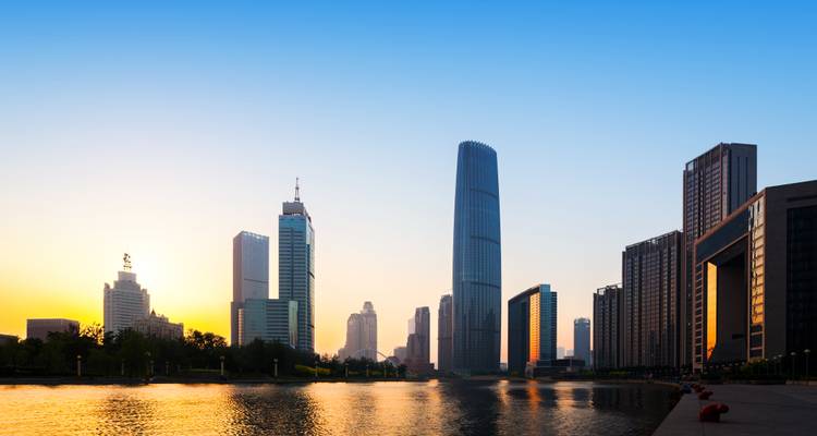 Moderne Stadtskyline mit Hochhäusern entlang eines ruhigen Flusses bei Sonnenaufgang