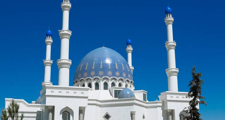 Opvallende witte en blauwe moskee met vier slanke minaretten staat tegen een wolkenloze azuurblauwe hemel in Asjchabad.