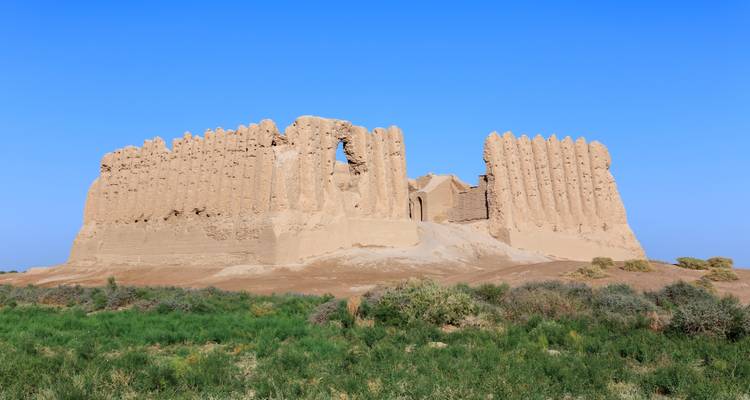Oude ruïnes van een moddersteenvesting rijzen op uit een lege vlakte onder een heldere blauwe Turkmeense hemel.