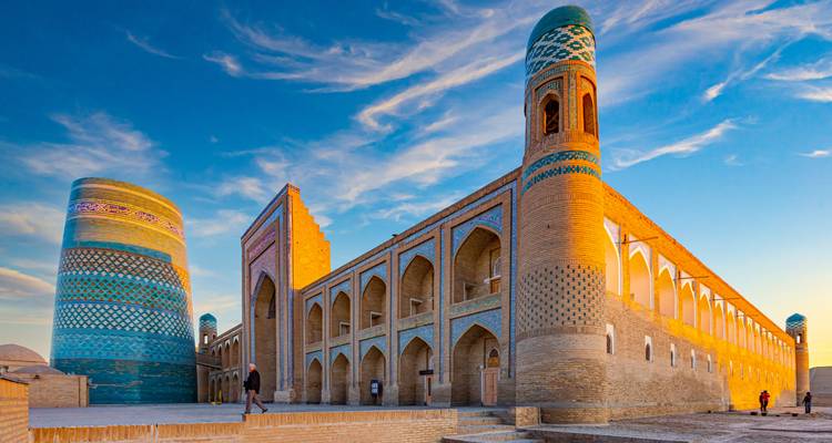 Kalta Minor's turkoois betegelde toren en aangrenzende madrasa gloeien in het gouden uur licht in Khiva.
