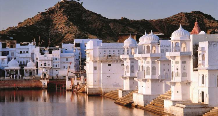 Weiße Gebäude mit Kuppeln an einem spiegelnden Gewässer bei Sonnenuntergang.